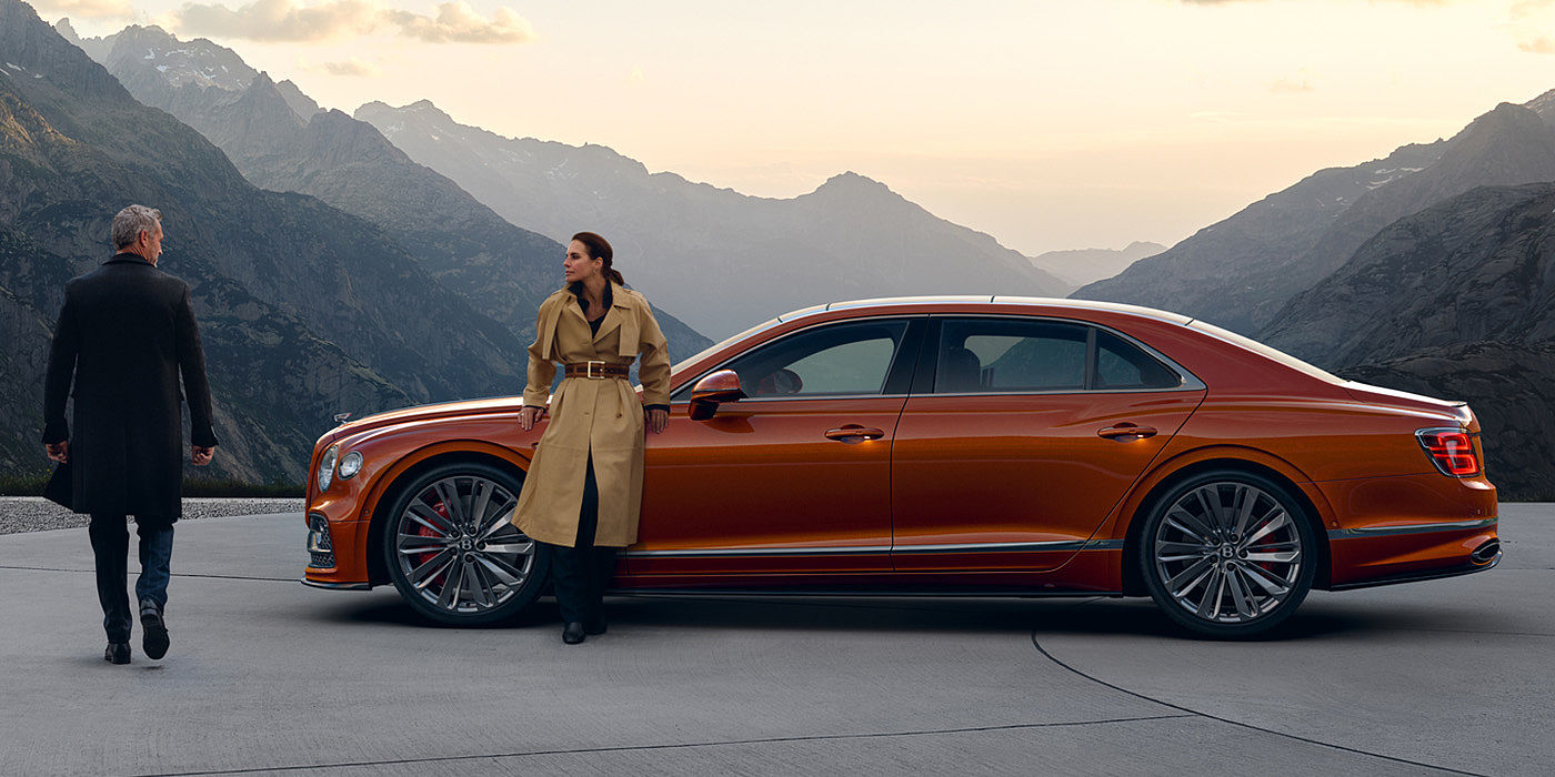 Bentley Santiago Bentley Flying Spur Speed parked in Orange Flame coloured exterior parked, with mountainous background and two people in view.