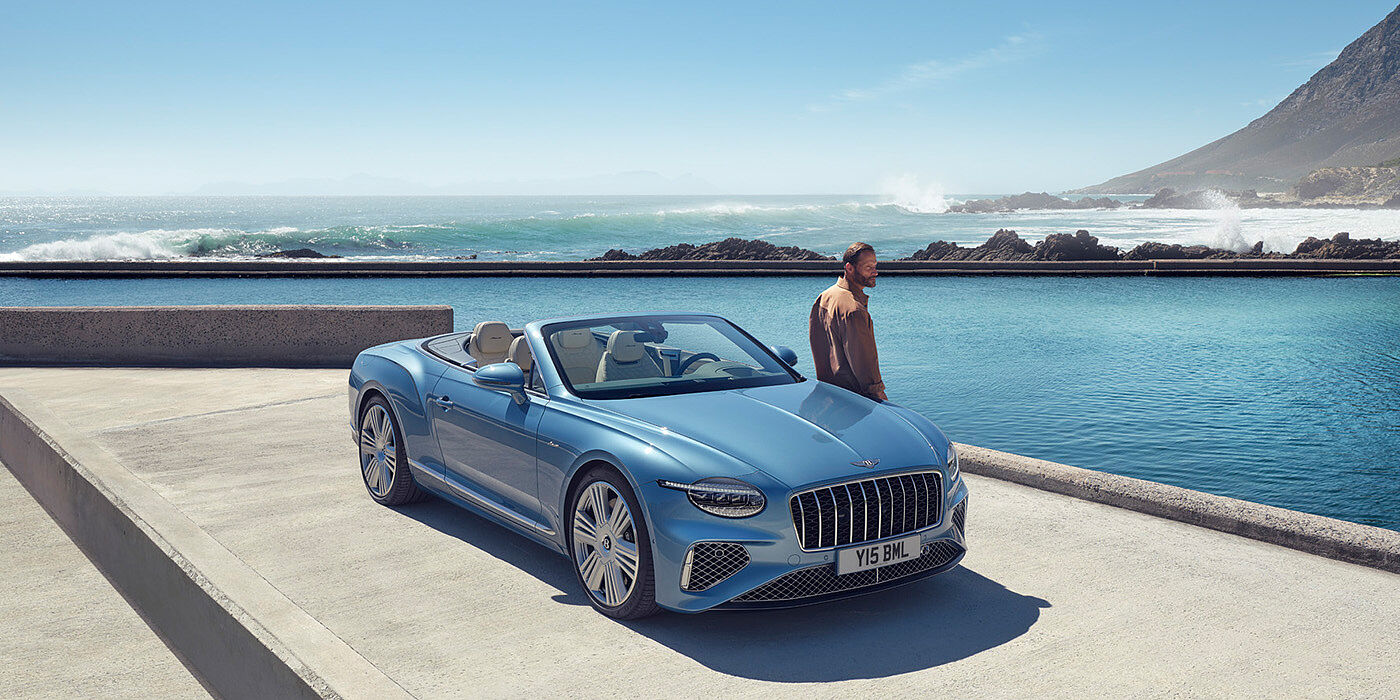 Bentley Santiago New Bentley Continental GTC Azure convertible front view in Light Windsor blue paint with 22 inch ten spoke wheels parked by the sea in the sunshine
