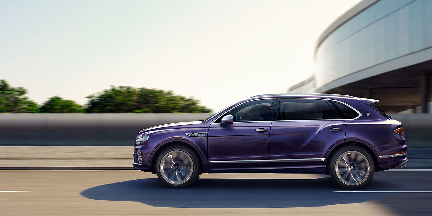 Bentley Santiago Bentley Bentayga Extended Wheelbase Mulliner luxury SUV profile in Tanzanite Purple paint, driving on an country road past trees.