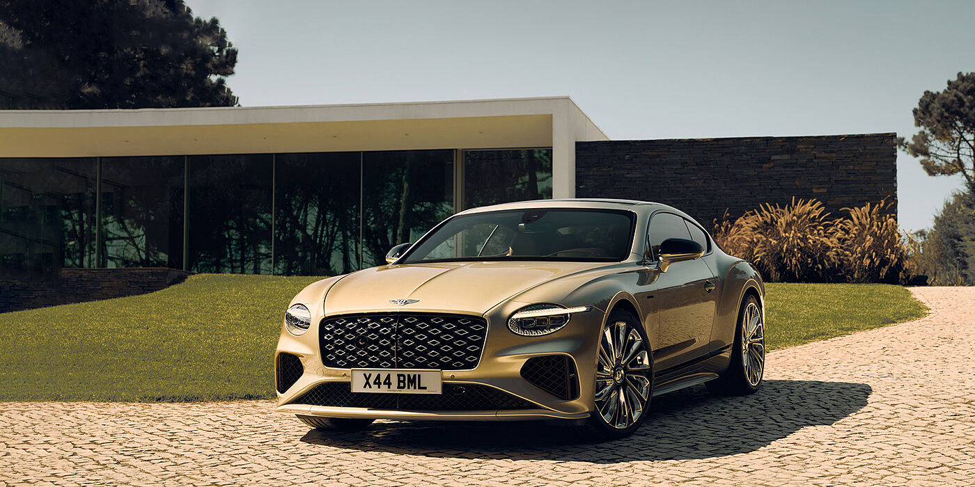 Bentley Santiago Bentley Continental GT Mulliner coupe front three quarters in Patina paint parked outside a glass fronted building with a grass lawn behind it