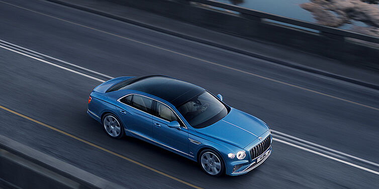 Bentley Santiago New Bentley Flying Spur Azure sedan in Light windsor blue paint by Mulliner, with 22 inch Azure wheels seen from overhead driving dynamically on a country road