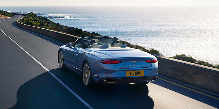 Bentley Santiago New Bentley Continental GTC Azure convertible rear view in Light Windsor blue paint with 22 inch ten spoke wheels driving dynamically on an ocean road in the sunshine